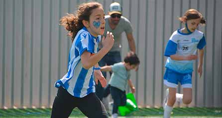 Student with a real shirt and a blue heart drawn on her face running, in the background more students running